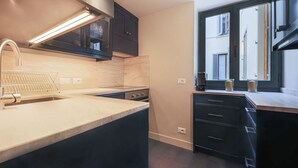 Cocina moderna con armarios oscuros, una campana extractora de acero inoxidable, un lavamanos y una ventana con vistas a edificios.