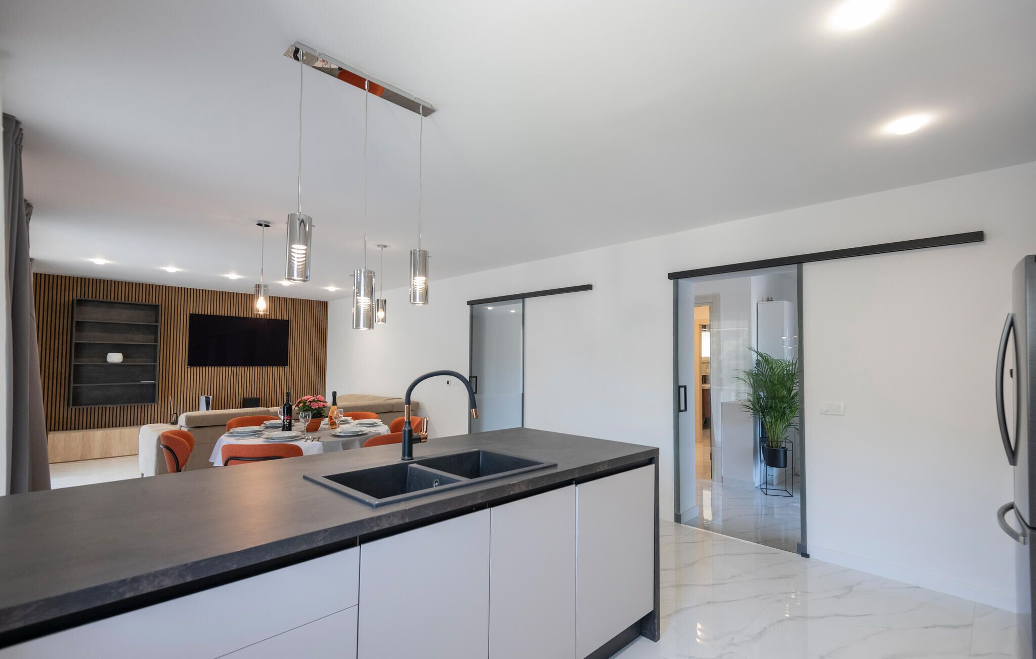 A modern kitchen with a central island, pendant lighting, and a sliding glass door leading to a dining area.