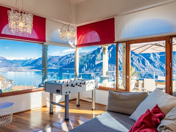 Una habitación con mesa de fútbol, ventanas amplias con vista a la montaña y una araña.