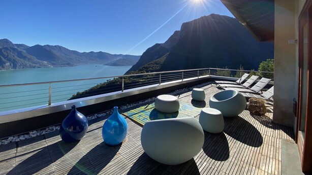 Une terrasse avec coin salon extérieur, offrant une vue sur un lac et des montagnes.