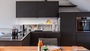 Eine moderne Küche mit dunklen Schränken, einem eingebauten Backofen und einem Essbereich mit Holztisch, gedeckt für eine Mahlzeit.