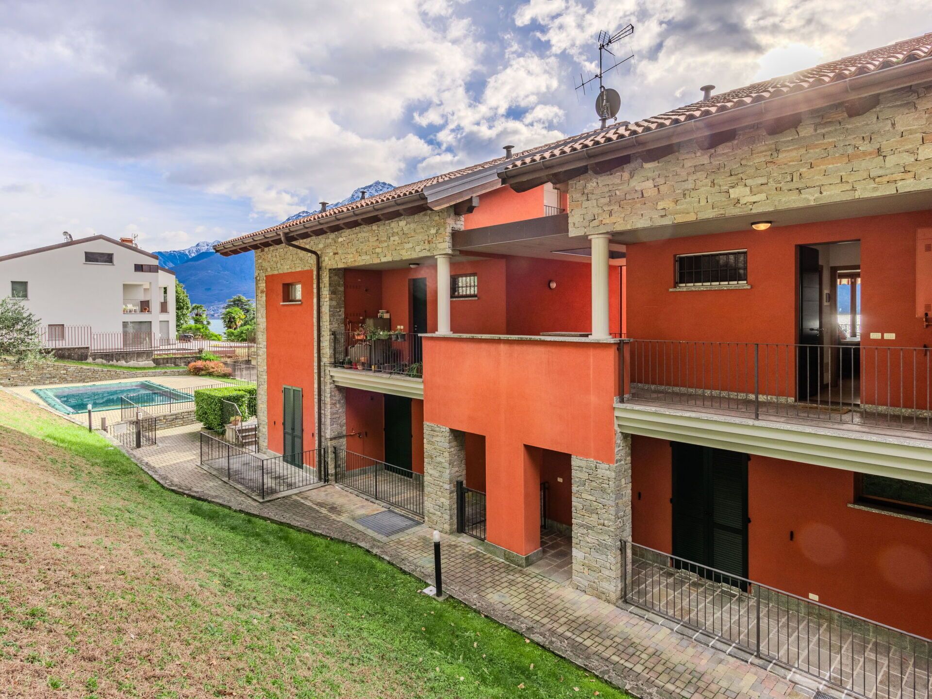 A two-story building with a swimming pool, balconies, and a stone facade.