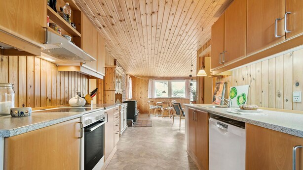 Eine moderne Küche mit Holzschränken, einer zentralen Kochinsel und einem Essbereich mit Tisch und Stühlen.