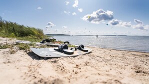 Ein Strand mit einem Surfbrett und Kopfhörern im Sand, ein klarer Himmel und eine entfernte Wasseransicht.