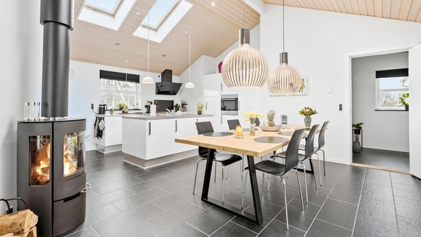 Una cocina moderna con una isla central, estufa de leña, tragaluces e iluminación colgante.