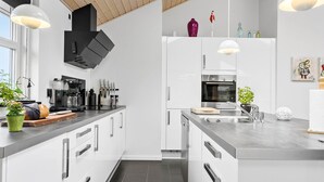 Una cocina moderna con armarios blancos, horno empotrado y cafetera.