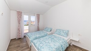 Ein Schlafzimmer mit zwei Betten, einem Fenster mit Vorhängen und Blick auf Gebäude sowie Wasser.
