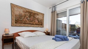 A hotel room with a large bed, two bedside tables with lamps, a large painting on the wall, and a view of the outside through a sliding glass door.