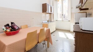 A compact kitchen with a dining table, chairs, a refrigerator, and a basket of groceries.