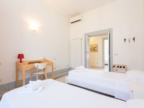 Een hotelkamer met twee bedden, een bureau, een stoel, een rode lamp en een deur naar een andere kamer.
