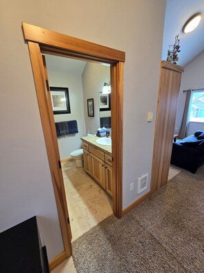 A hallway leading to a bathroom with a toilet, sink, and cabinets. - Water Lover's Paradise (Rockaway Beach)