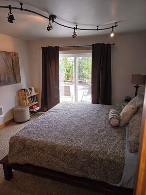 A bedroom with a large bed, a bookshelf, a window with curtains, and a ceiling light fixture. - Water Lover's Paradise (Rockaway Beach)