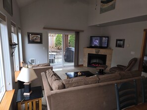 Una sala de estar con sofá, televisión, chimenea y un área de comedor visible a través de una puerta de vidrio.