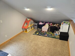 Ein Zimmer mit einem Spielhäuschen, Spielzeug und einem Teppich.