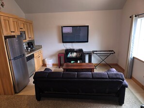 Ein gemütlicher Wohnbereich mit Küchenzeile, einem Wand-Fernseher, einer Couch und einem kleinen Tisch.