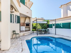 Ein Swimmingpool mit einer Pergola, Sitzgelegenheiten im Freien und einer Grillzone.