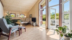 A cozy living room with wooden walls and large windows, a grey sofa, a chair, a TV, and a potted plant. - Beautiful home in Tarm with WiFi (Tarm)
