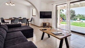 A modern living room with a sofa, a coffee table, and a dining area with chairs and a TV. - Wonderful private villa for 8 people with A/C, WIFI, private pool, TV and terrace (Albufeira)