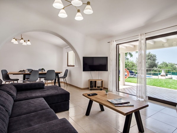 A modern living room with a sofa, a coffee table, and a dining area with chairs and a TV.