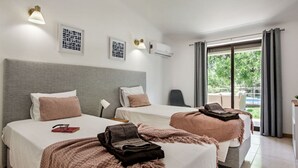 A hotel room with two beds, a grey headboard, a small desk, and a window with a view of greenery. - Wonderful private villa for 8 people with A/C, WIFI, private pool, TV and terrace (Albufeira)