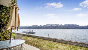 Un patio con una mesa y sillas, una sombrilla y vistas a un lago con montañas al fondo.