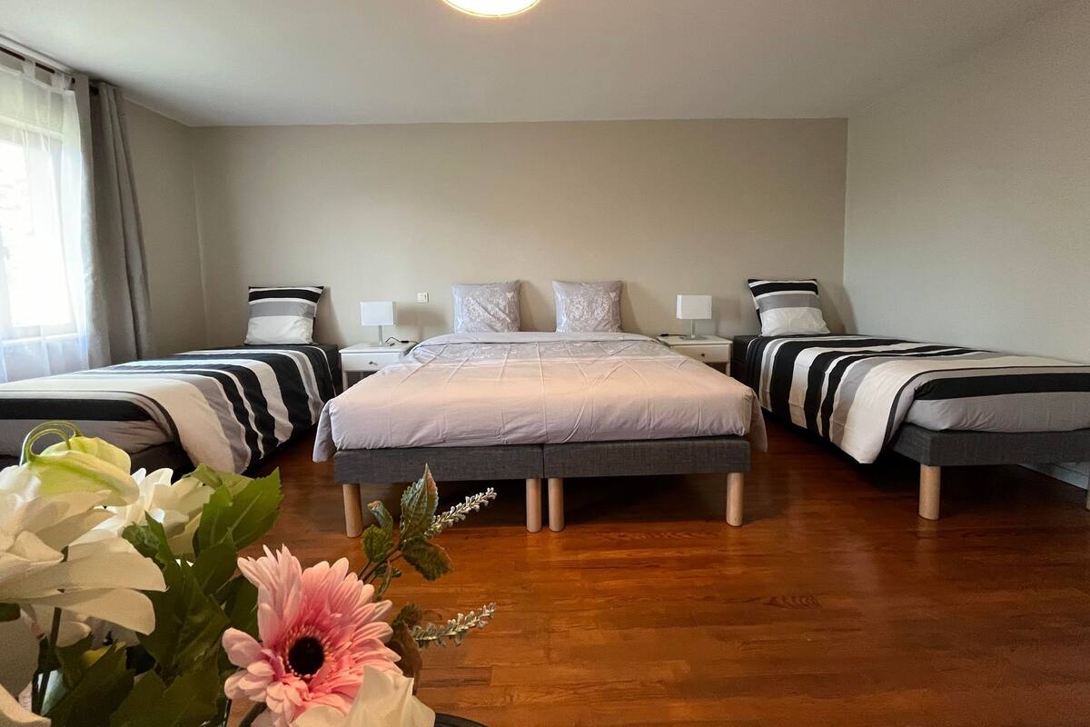A hotel room with two single beds, a large bed, a bedside table with a lamp, and a wooden floor.