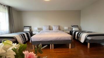 A hotel room with two single beds, a large bed, a bedside table with a lamp, and a wooden floor.