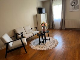 Una sala de estar con un sofá, una mesa de centro con un jarrón de flores, un televisor sobre un mueble bajo y un radiador.