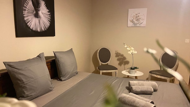 A hotel room with a large bed, two chairs, a small table, and a potted orchid. - Gite le Saint André (Villers-sur-Port)
