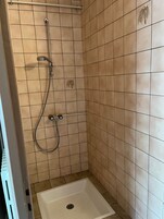 Un área de ducha pequeña con azulejos, y un cabezal de ducha y un rociador de mano.