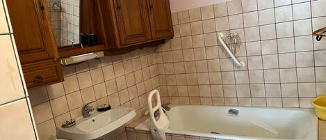 Un baño con lavamanos, inodoro y bañera. Hay armarios de madera sobre el lavamanos y un espejo.