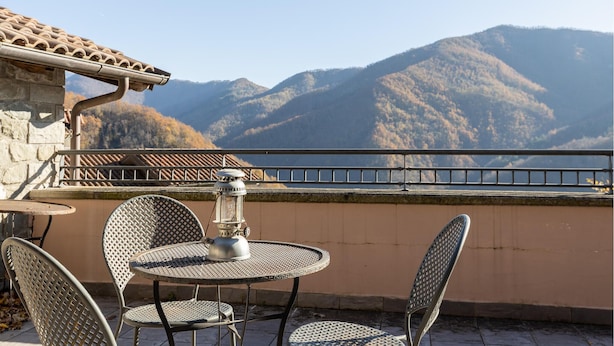 Een terras met een ronde metalen tafel en stoelen, een metalen lantaarn en uitzicht op bergen.