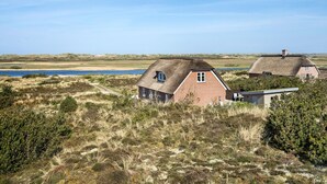 A thatched-roof house with a brick extension, surrounded by natural landscape and a body of water. - Awesome home in Nørre Nebel (Nørre Nebel)