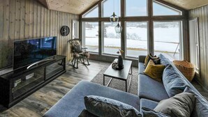 Un salón acogedor con una televisión grande, asientos cómodos y vistas a un paisaje nevado a través de amplios ventanales.