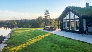 Una casa moderna con fachada de vidrio, jardín con césped y una mesa de picnic.