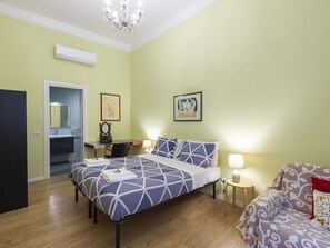 Een slaapkamer met een bed, nachtkastje, lamp en een sofa.