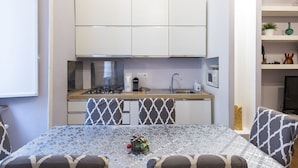A compact kitchen with white cabinets, a gas stove, and a microwave. There is a dining table with patterned chairs and a decorative centerpiece. - Nice apartment for 9 guests with A/C, WIFI and TV (Rome)
