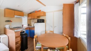 Eine kompakte Küche mit Herd, Mikrowelle und Kühlschrank, ein Esstisch mit Stühlen und ein Fenster mit Vorhängen.