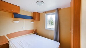 Ein Schlafzimmer mit Bett, Holz-Kopfteil, Einbauschränken und einem Fenster mit Vorhängen.