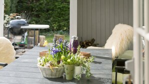 Une terrasse en bois agrémentée de plantes en pot, d’un barbecue et d’une chaise blanche.