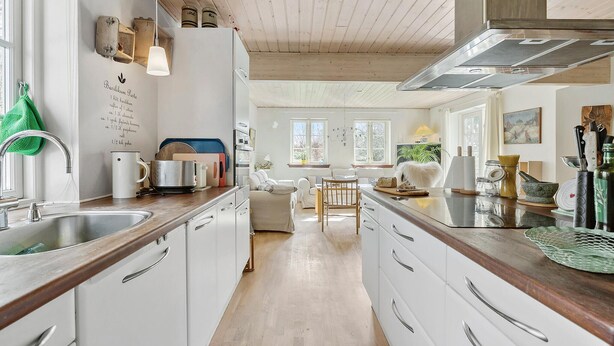 Une cuisine moderne avec des armoires blanches, des plans de travail en bois et un îlot central. On y trouve divers appareils de cuisine et ustensiles sur les plans de travail.