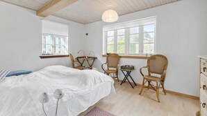 Une chambre à coucher avec un lit, deux fauteuils en osier, une petite table et une fenêtre donnant sur un paysage verdoyant.