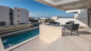 A modern outdoor pool area with a clear view of the sea, a bar area with seating, and a stone wall. - Nice home in Novalja with sauna (Novalja)