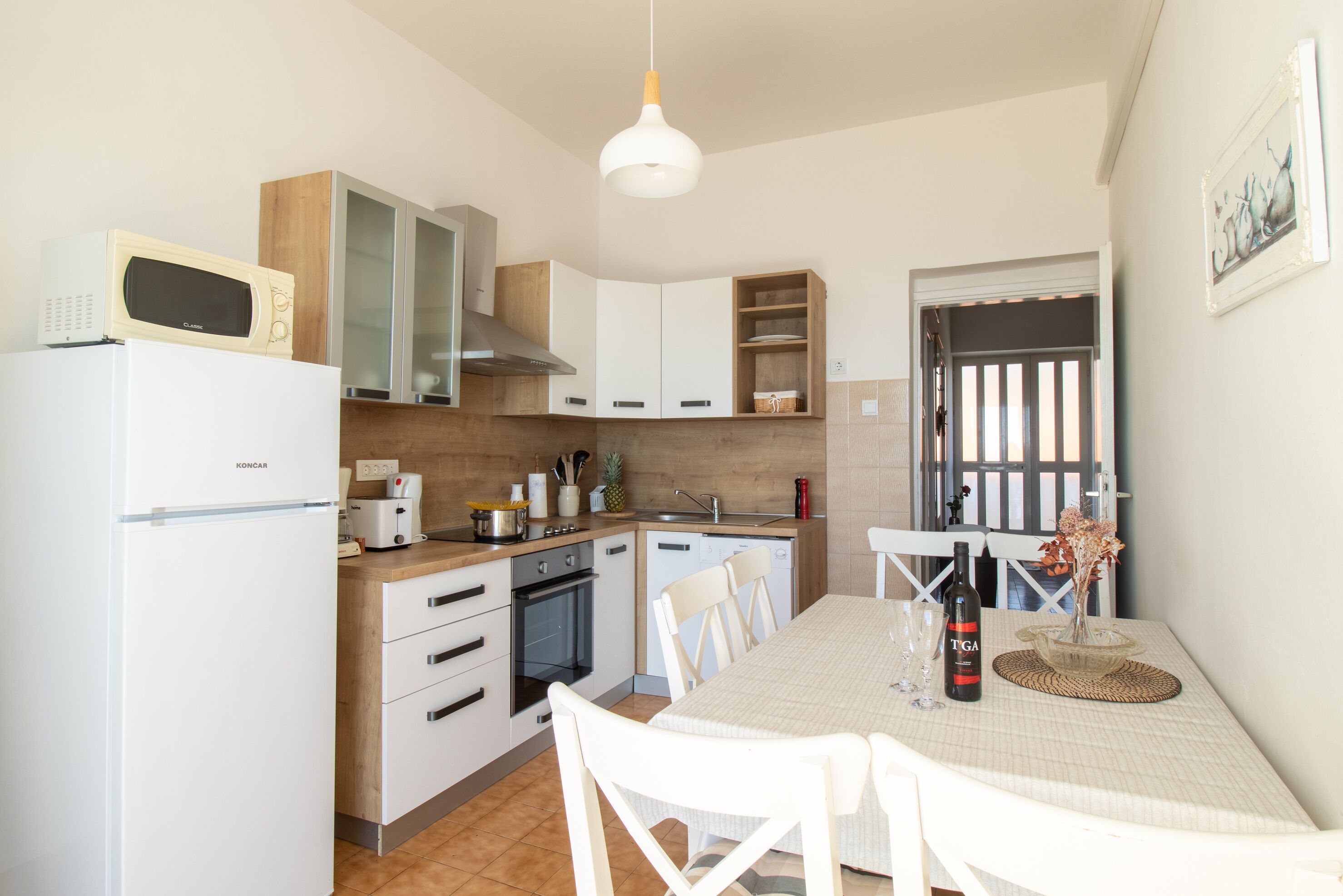 Cozinha moderna com armários brancos, micro-ondas, fogão e área de refeições com mesa e cadeiras.