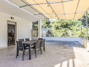 Une terrasse extérieure avec une table et des chaises, un espace abrité et une vue sur les arbres.