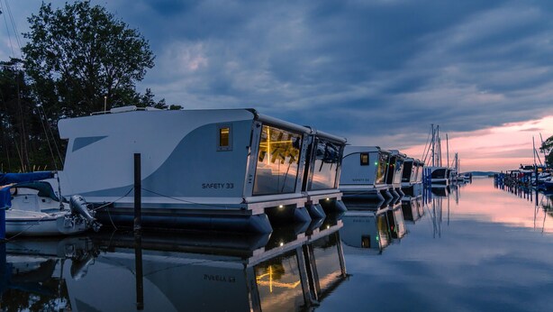 A row of boats docked at a marina with calm water reflecting the boats and the sky.