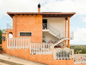 A two-story building with a balcony, a staircase, and a view of the countryside.