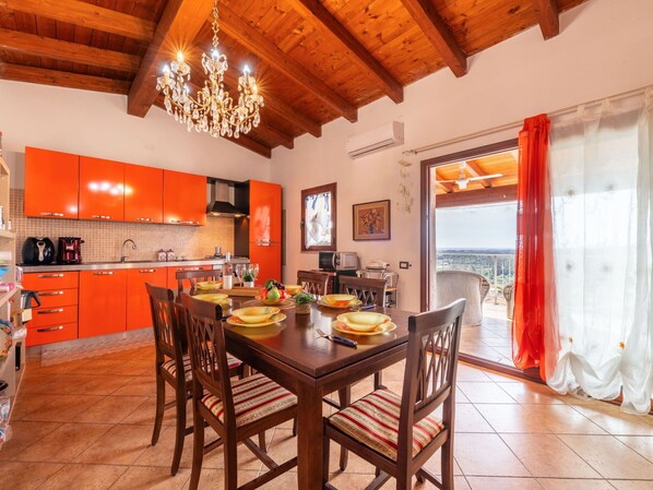 A dining area with a wooden table and chairs, a chandelier, and a kitchen with orange cabinets.