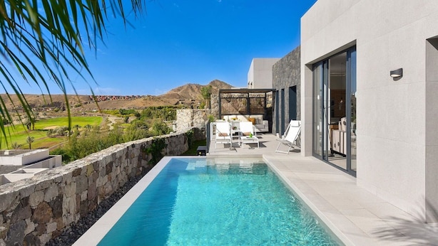 A modern outdoor pool area with a stone wall, lounge chairs, and a view of the landscape.