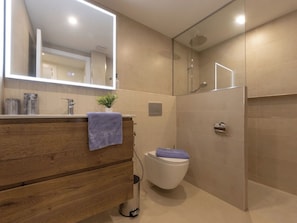 A modern bathroom with a wooden vanity, a mirror, a toilet, and a shower area.
